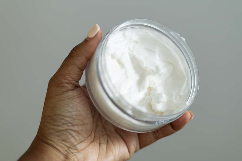 Close-up of hands holding a retinol cream jar beside before-and-after skin photos